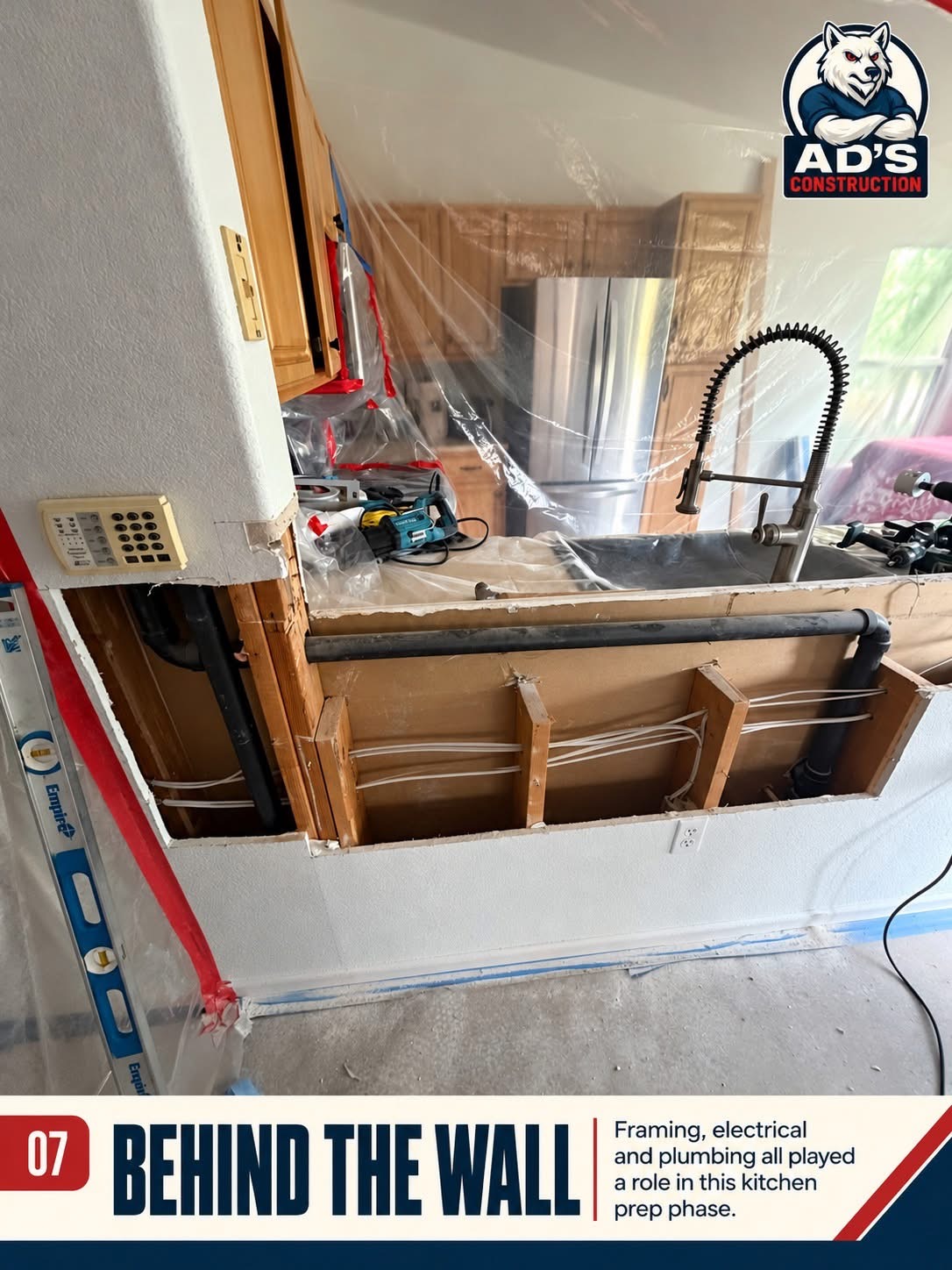 Opened kitchen half wall showing framing, electrical wiring and plumbing drain lines during prep